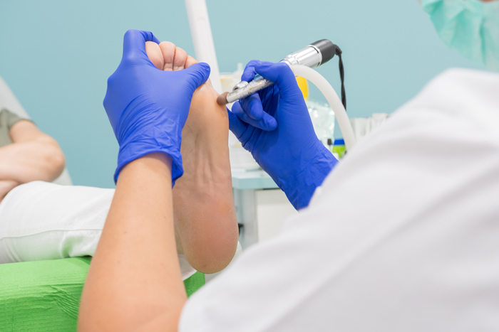 Female chiropodist, attending elder in a clinic and performing podiatric treatments